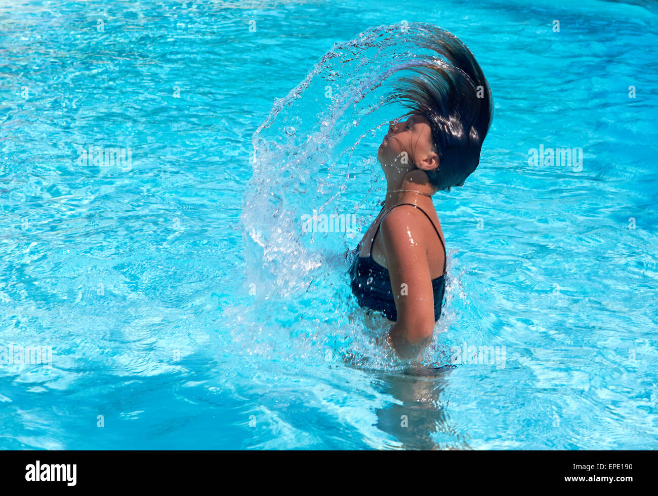 Pretty teen girl whipping her hair back in the pool and spraying water everywhere Stock Photo