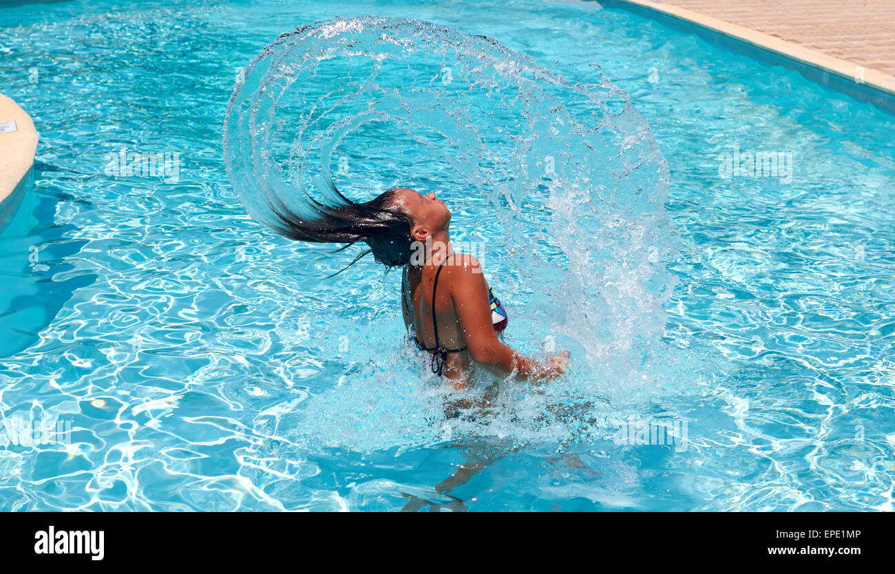 Pretty teen girl whipping her hair back in the pool and spraying water everywhere Stock Photo