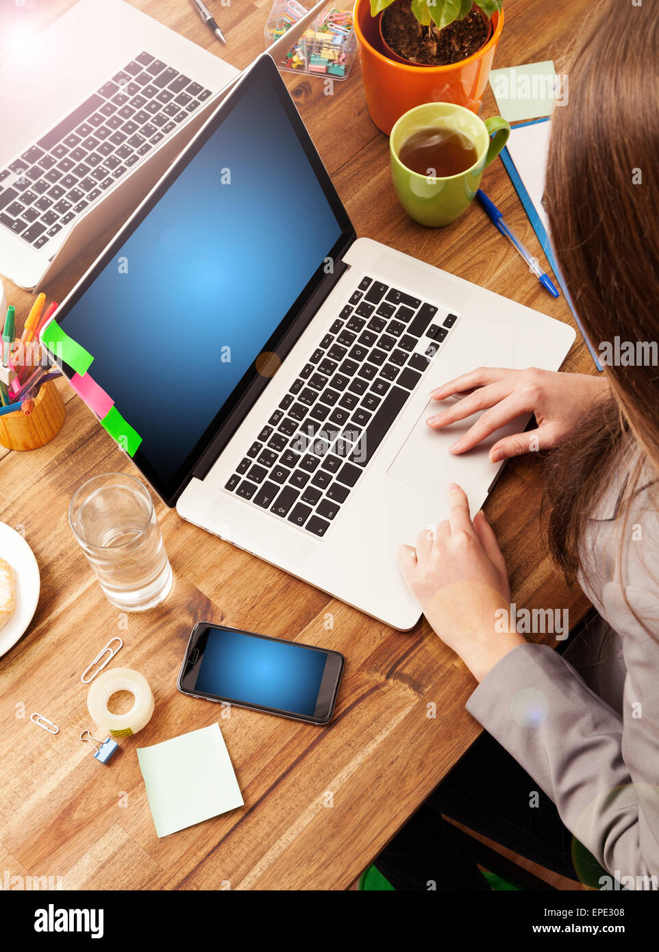 Young woman working with laptop placed on wooden desk with blank screen for text. Shot from aerial view Stock Photo