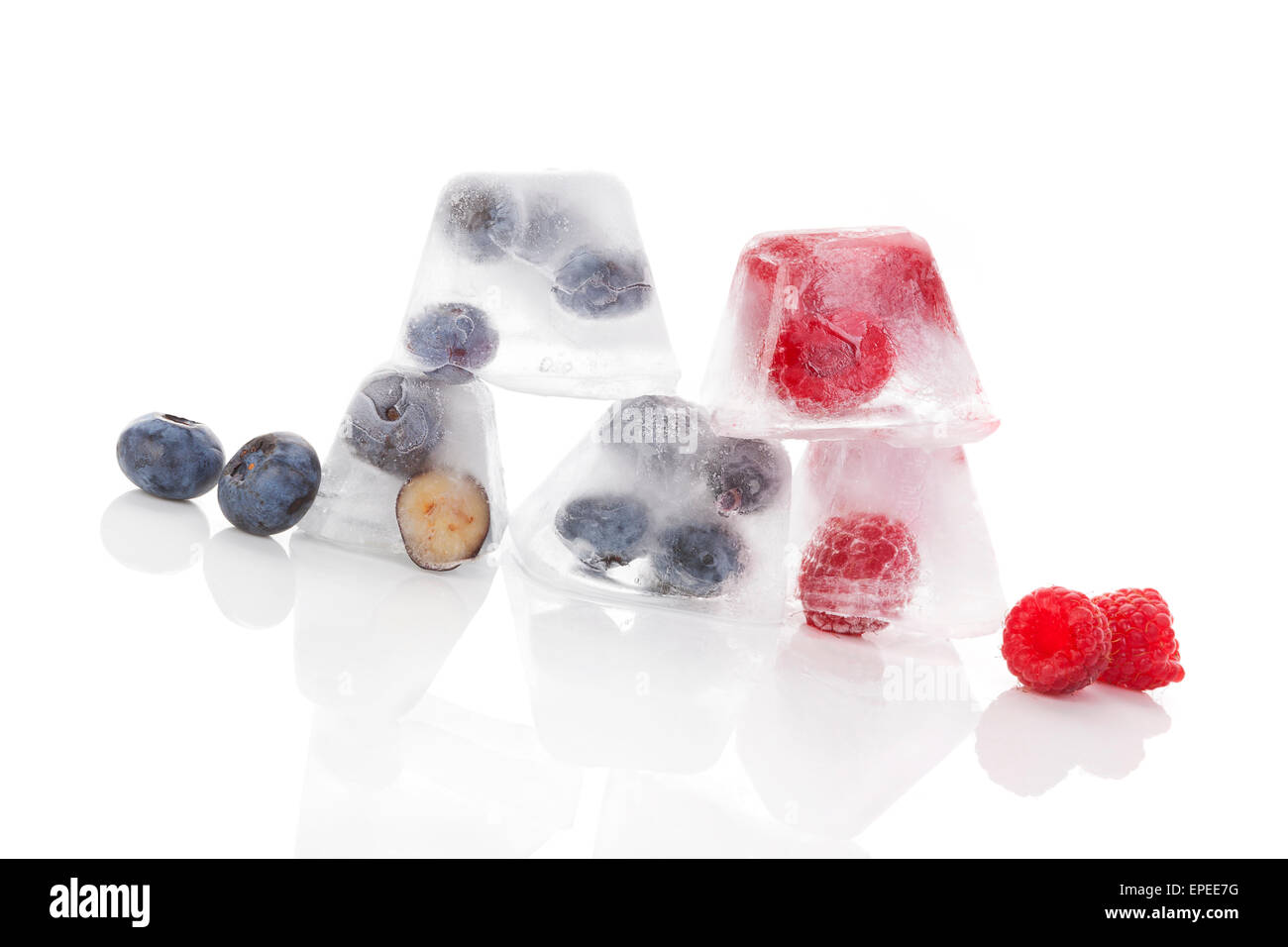 Fresh ripe fruits frozen in ice. Blueberries and raspberries in ice cubes isolated on white background. Fresh summer fruit Stock Photo