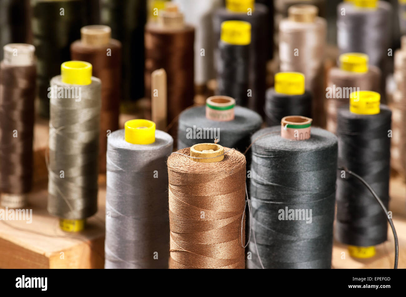 Background view of various colored yarns on bobbins at a tailor or clothing design studio in shades of gray and browns Stock Photo