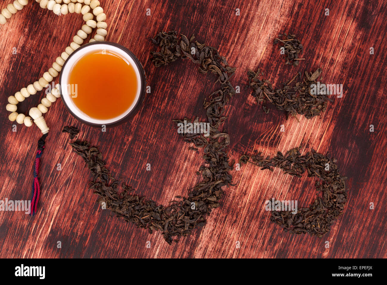 Cup of tea, dry tea leaves forming ohm symbol and buddhist necklace. Traditional tea drinking. Stock Photo