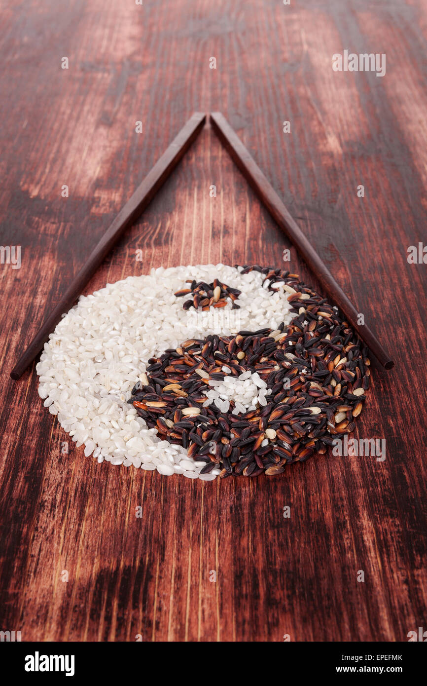 White and wild rice shaped as Yin yang symbol with chopsticks on dark ...