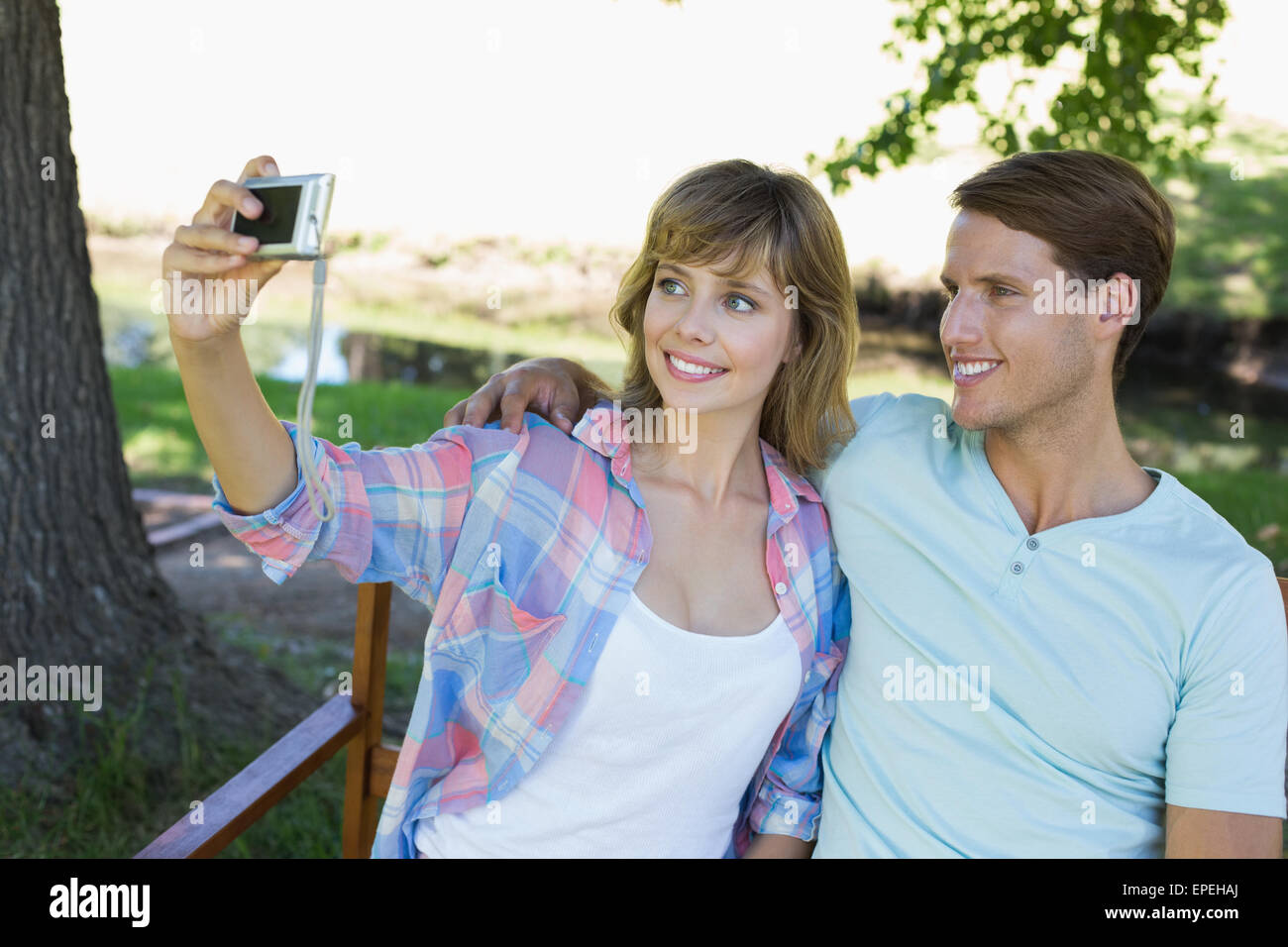 Cute couple sitting on bench in the park taking a selfie Stock Photo ...