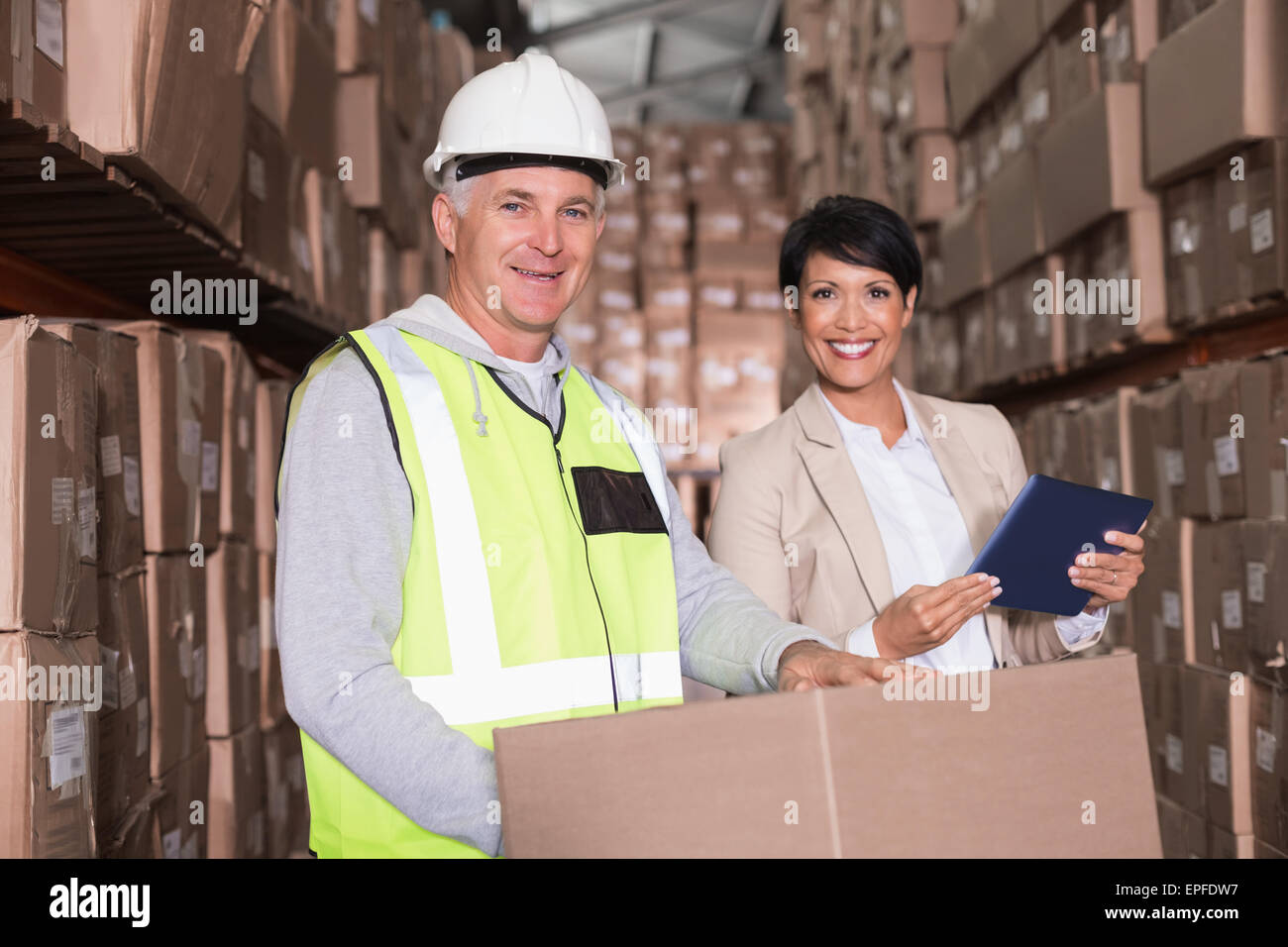 Warehouse worker moving boxes on trolley talking to manager Stock Photo