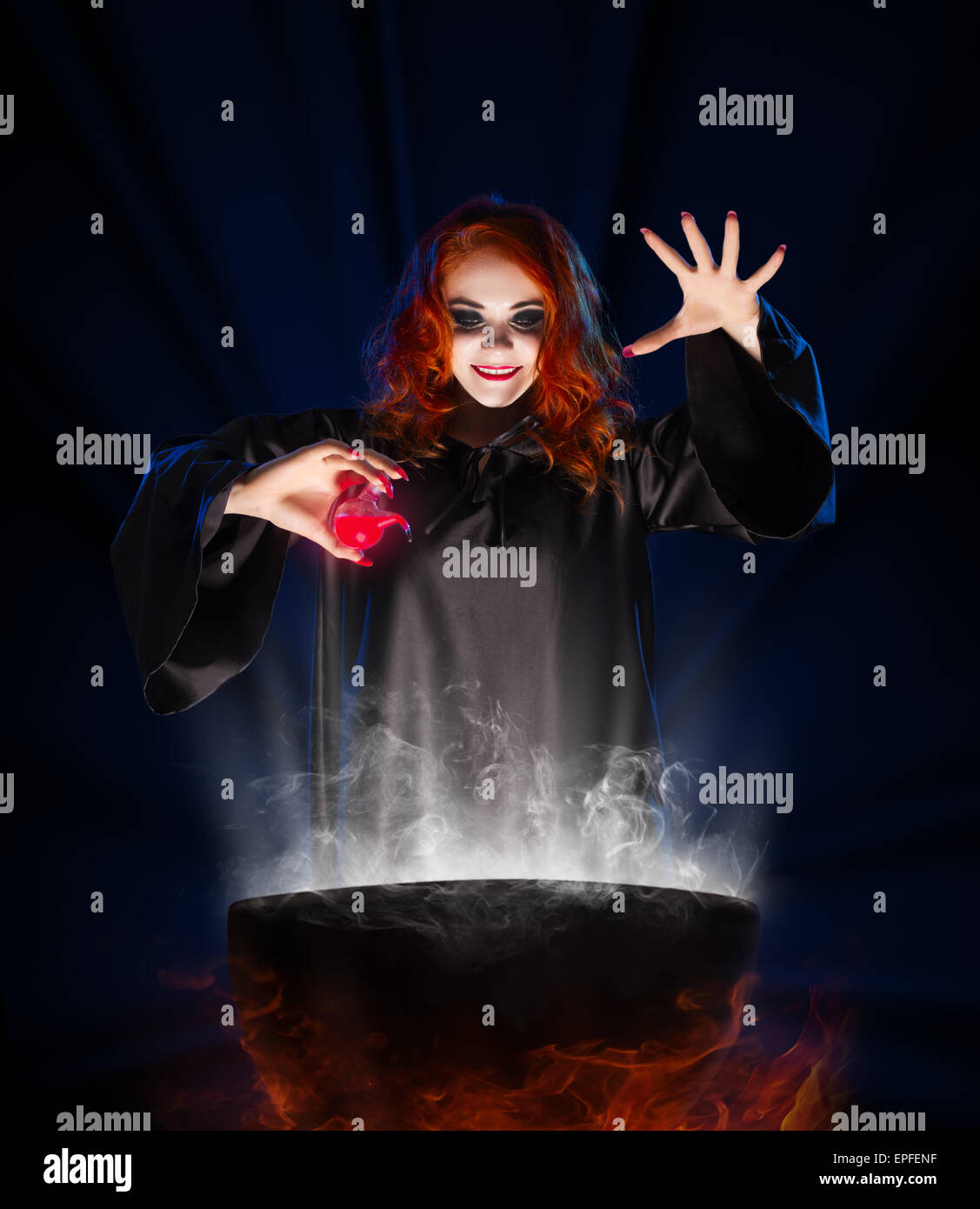 Young witch with red potion on blue rays background Stock Photo