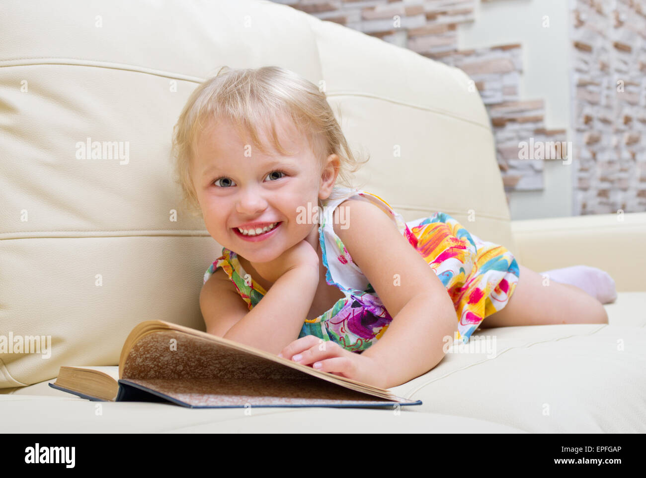 Little girl with book on sofa Stock Photo - Alamy