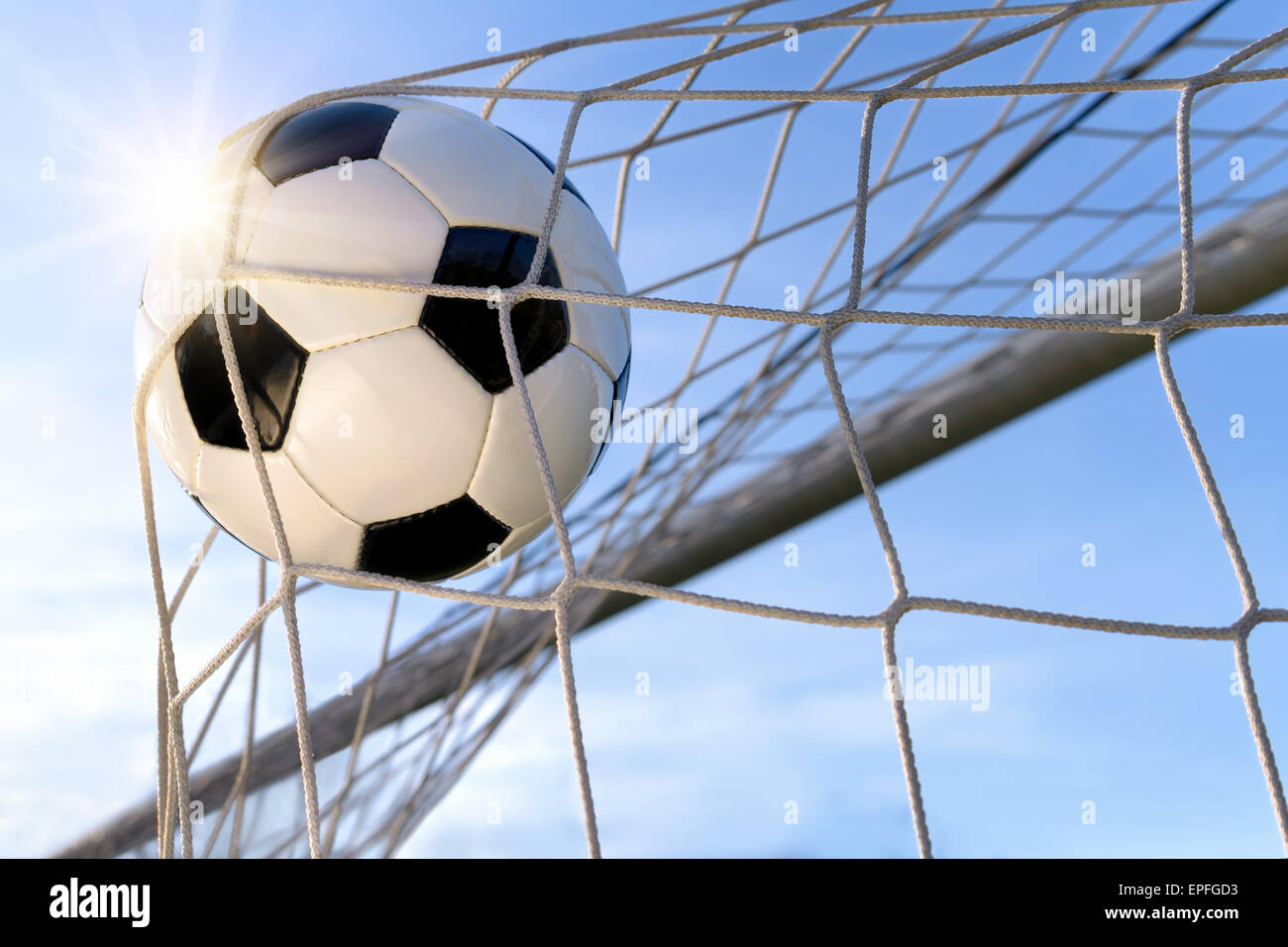 Football or soccer goal, with a neutral design ball flying into the net, blue sky and sun in the background Stock Photo