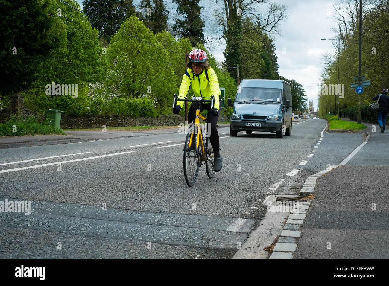A woman cyclist wearing a hi-vis jacket and crash helmet cycling on the road out of Cirencester, Gloucestershire, England UK Stock Photo