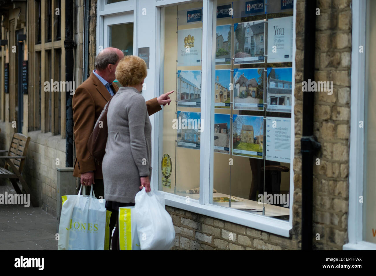 A middle-aged couple  looking at house prices in the window of Hamptons International  estate agents Cirencester, Gloucestershire, England UK Stock Photo