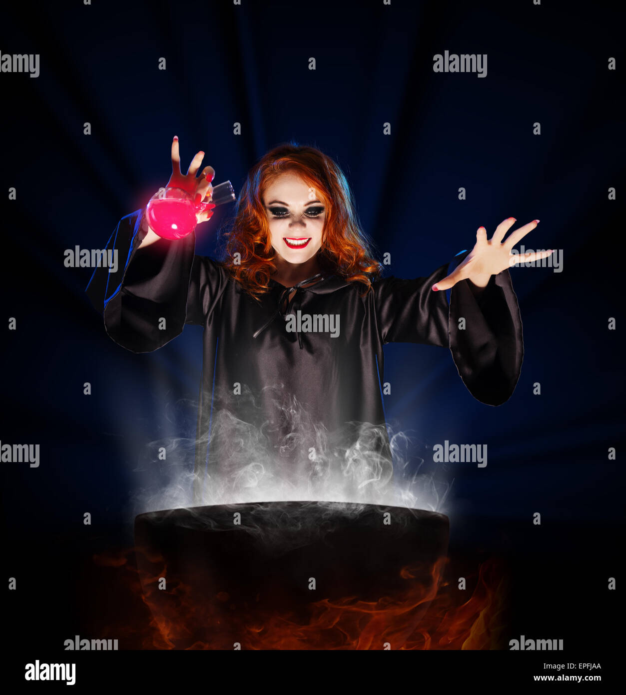 Young witch with potion and cauldron on blue rays background Stock Photo
