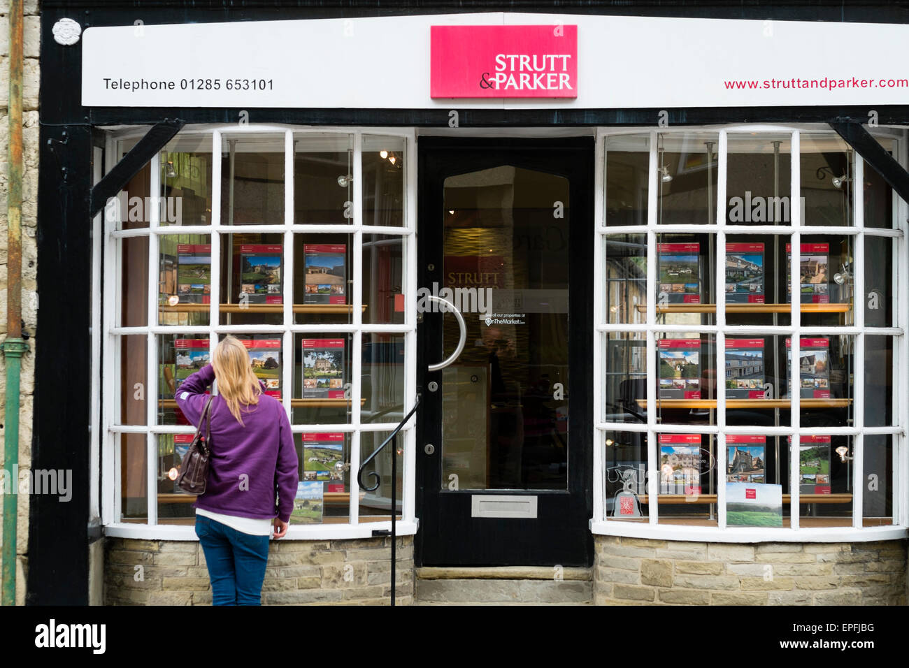 A woman looking at house prices in the window of Strutt and Parker estate agents Cirencester, Gloucestershire, England UK Stock Photo