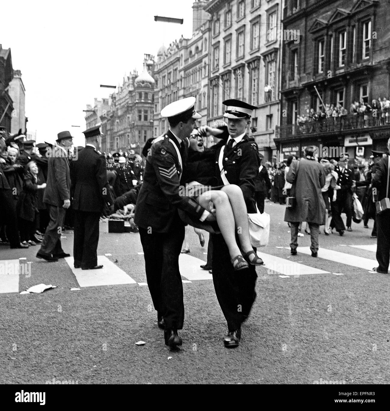 Northern premier of The Beatles film 'A Hard Day's Night'. Police try to control the fans in the streets of Liverpool, pictured here 2 police men carry an injured fan. 10th July 1964. Stock Photo