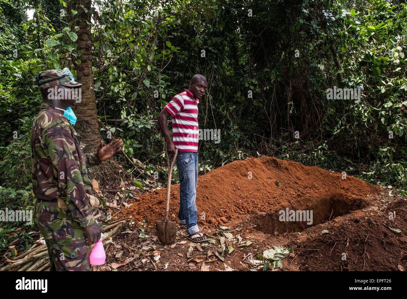 A soldier looks on as a man stands by a grave where a suspected Ebola victim is about to be buried. Eastern Sierra Leone was a hot spot for Ebola for several months, but eventually authorities managed to bring down infection rates to just a few cases per week. It showed that even after Ebola takes hold, it can be brought under control. But a recent spike in Kenema caused by unsafe burial practices demonstrates how quickly things can change.The outbreak is the world's largest, and has killed over 4,500 people in three countries in West Africa. Komende Luyama, Sierra Leone. 17/10/2014. (Tommy Tr Stock Photo