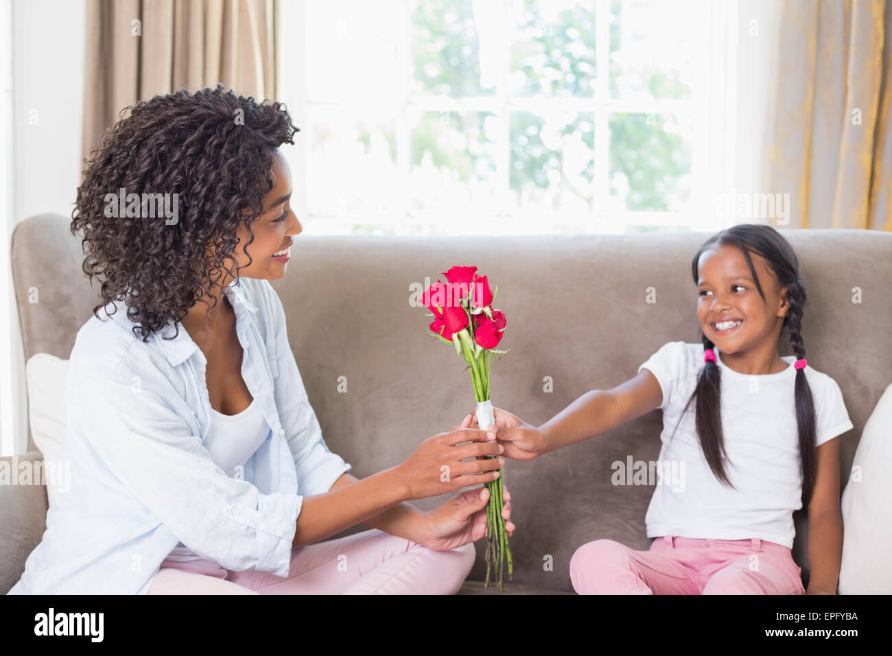 Pretty mother sitting on the couch with her daughter offering roses ...