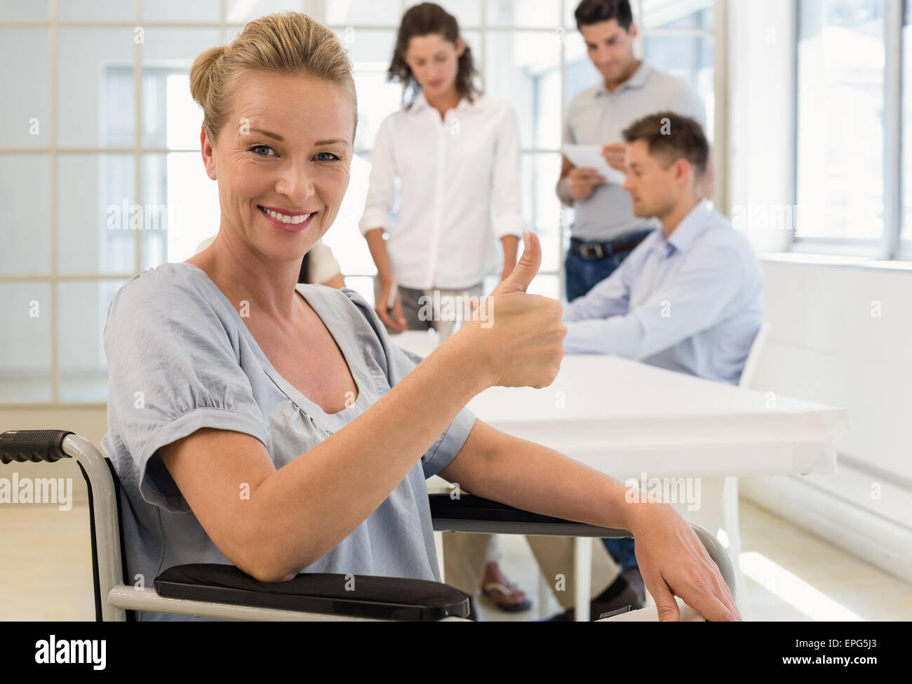 Casual businesswoman in wheelchair smiling at camera with team behind ...