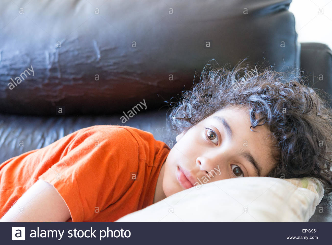 Latin Toddler Boy With Curly Hair Lying Down On A Black Couch With