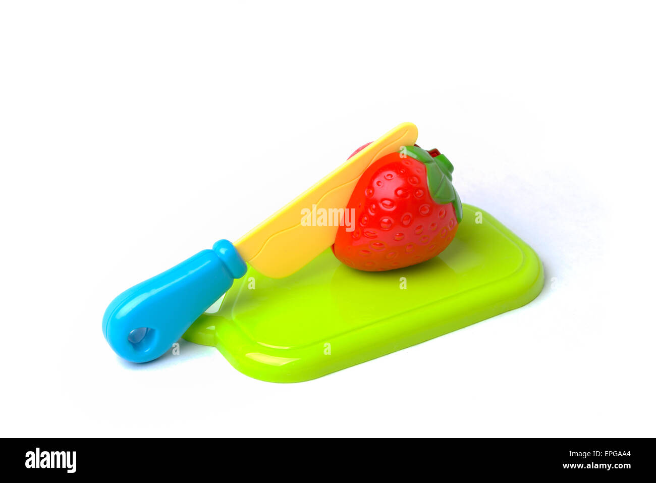 A plastic toy strawberry on a cutting board being cut in half with a