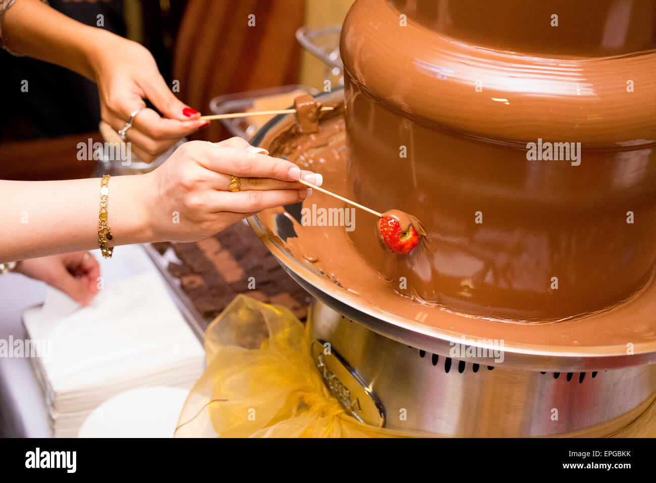 hands dipping snacks into a chocolate fountain Stock Photo