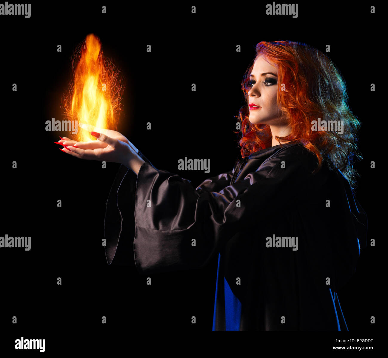 Young witch girl holds fire isolated on black Stock Photo