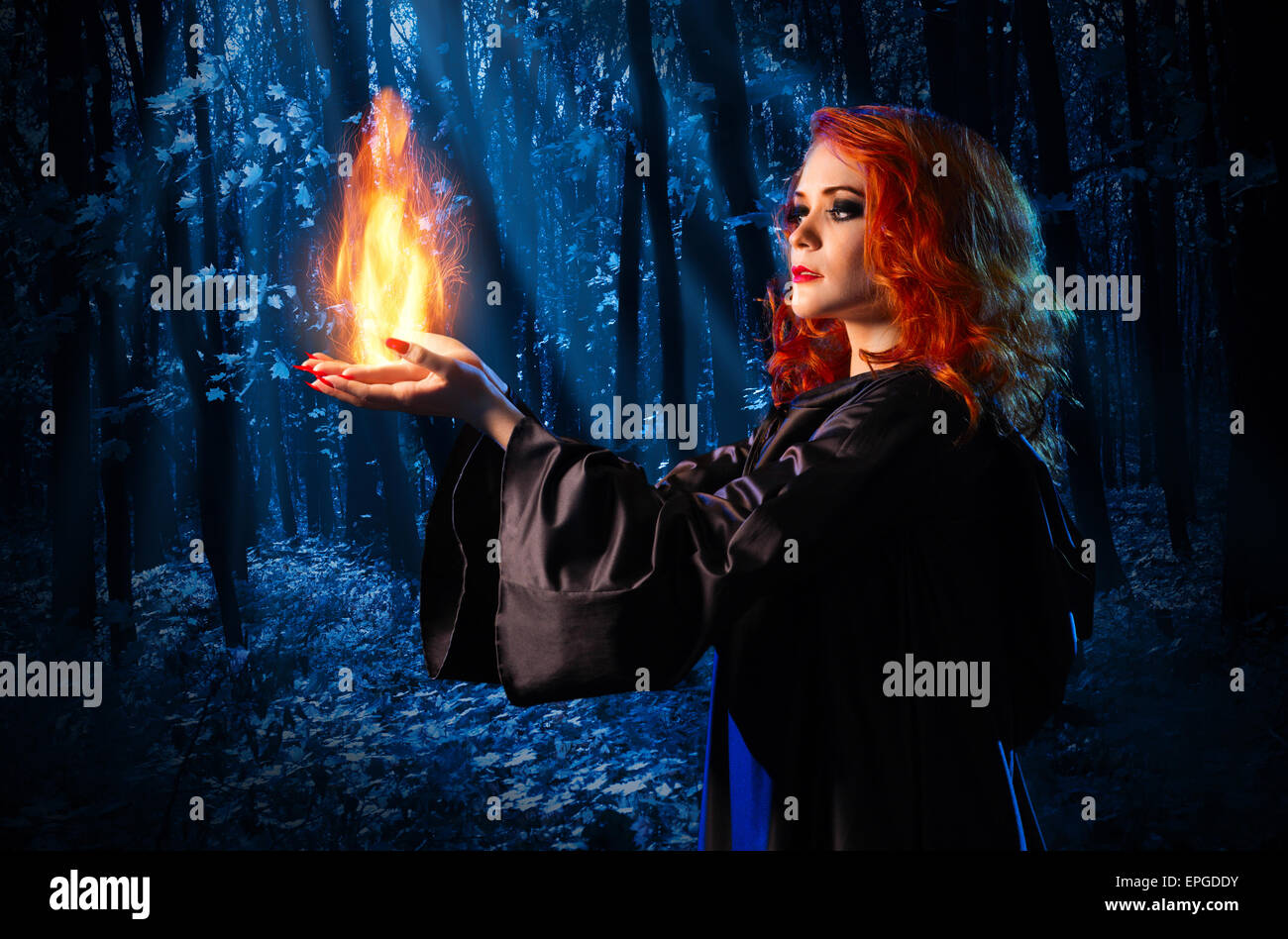 Young witch in the night forest holds fire Stock Photo