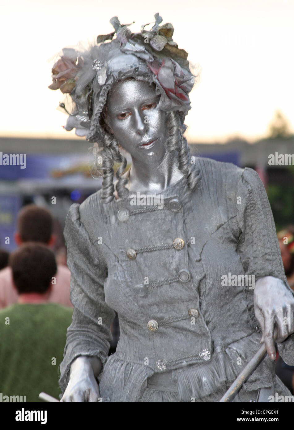 Close up of a young woman coated in silver and playing a drum as she performs as a living statue for tips in Asheville, NC Stock Photo