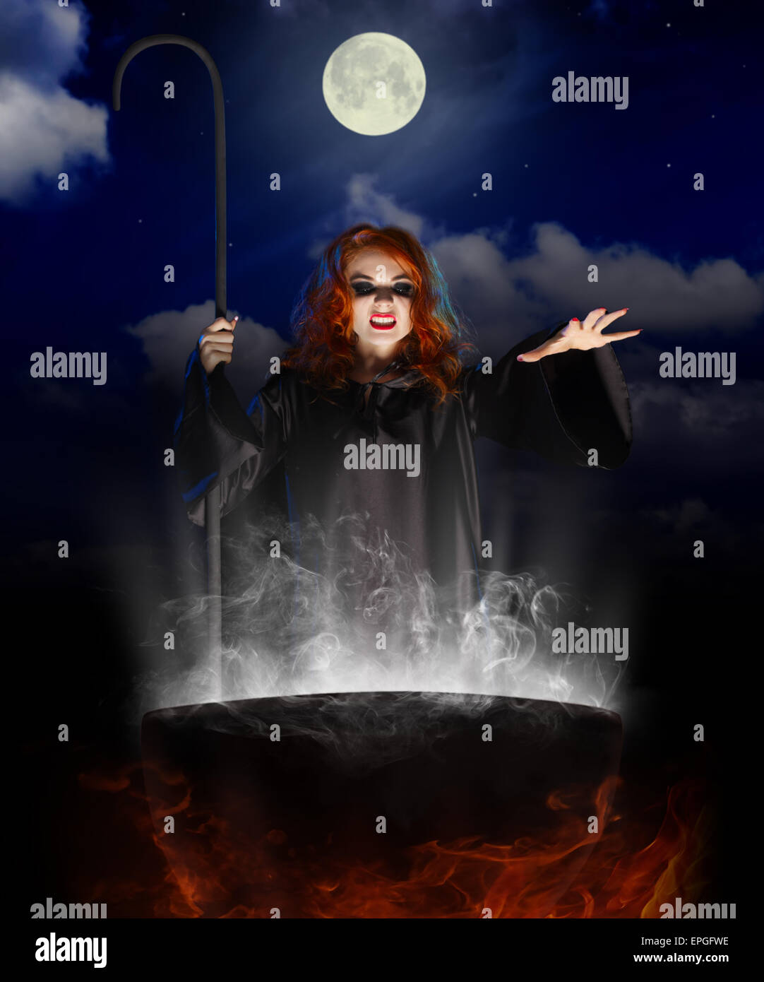 Young witch with cauldron on night sky background Stock Photo