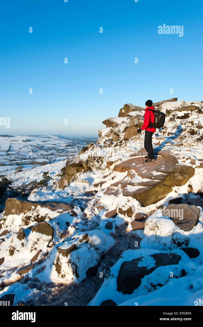 Walker in snow admiring view of Bosley Cloud & Cheshire from The Roaches, Peak National Park, Staffordshire, England. Stock Photo