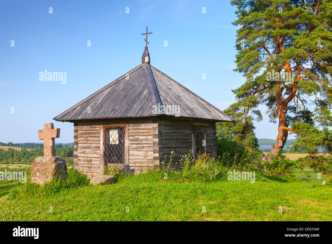 Ancient small wooden Orthodox chapel and stone cross on Savkina gorka, Pskov Region, Russia Stock Photo