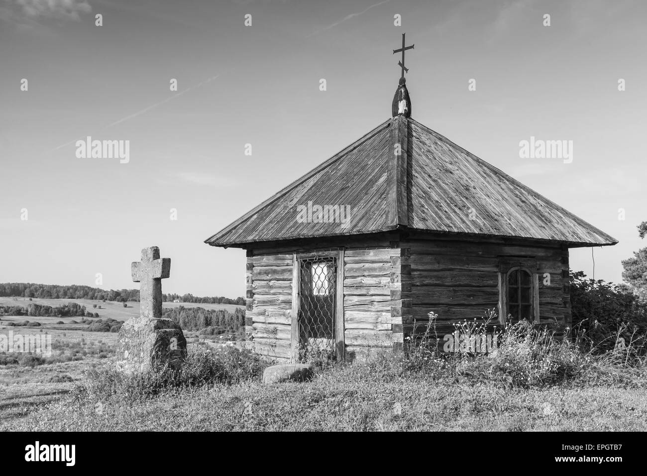 Ancient wooden Orthodox chapel and a stone cross on Savkina gorka, Pskov Region, Russia. Black and white photo Stock Photo