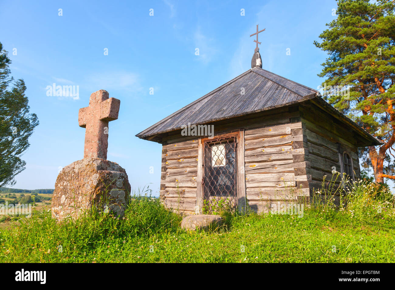 Ancient small wooden Orthodox chapel and a stone cross on Savkina gorka, Pskov Region, Russia Stock Photo