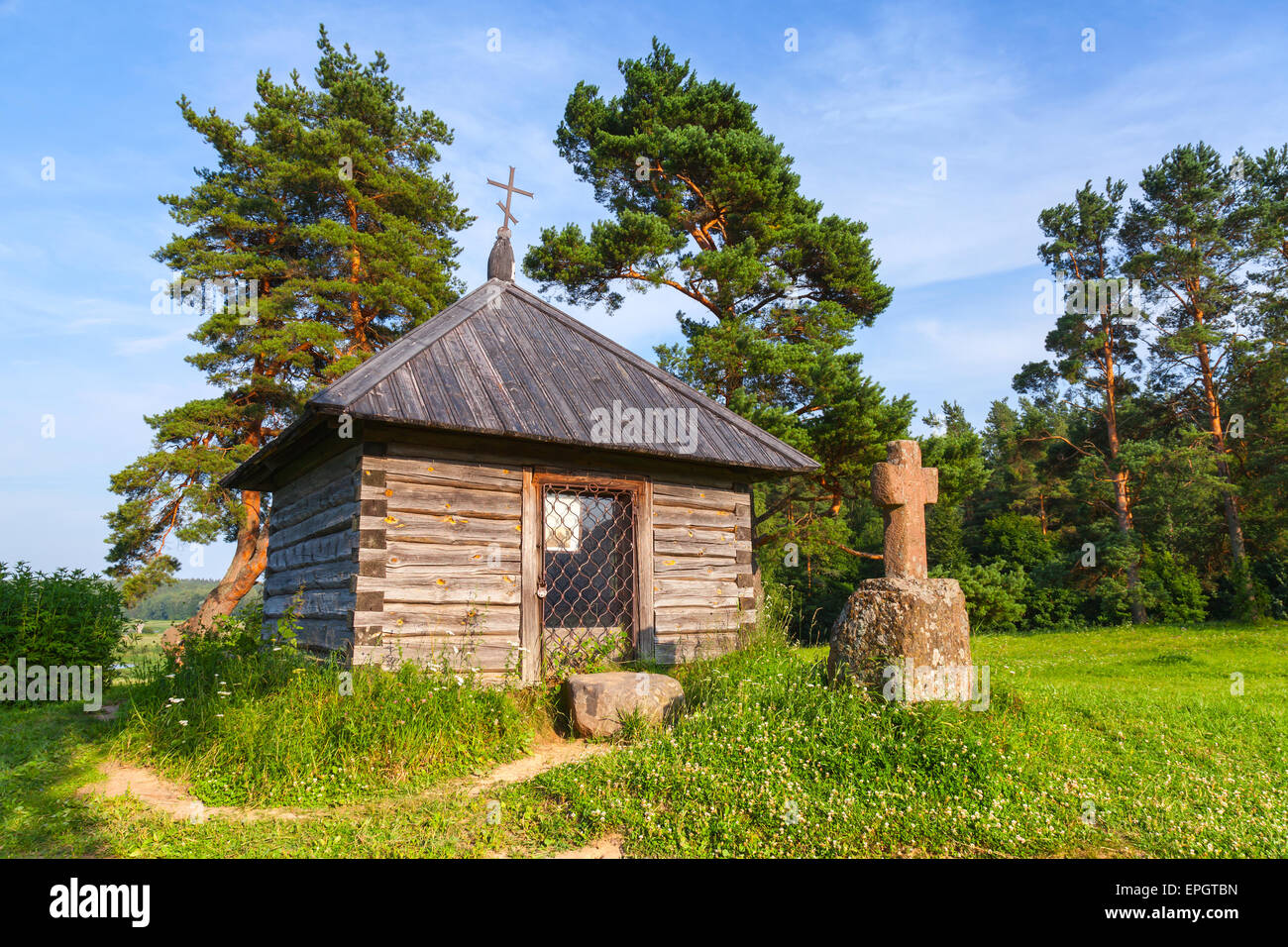 Ancient wooden Orthodox chapel and a stone cross on Savkina gorka, Pskov Region, Russia Stock Photo
