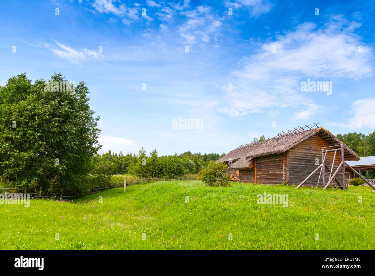Russian rural landscape with old wooden barns on green hills under bright blue cloudy sky Stock Photo