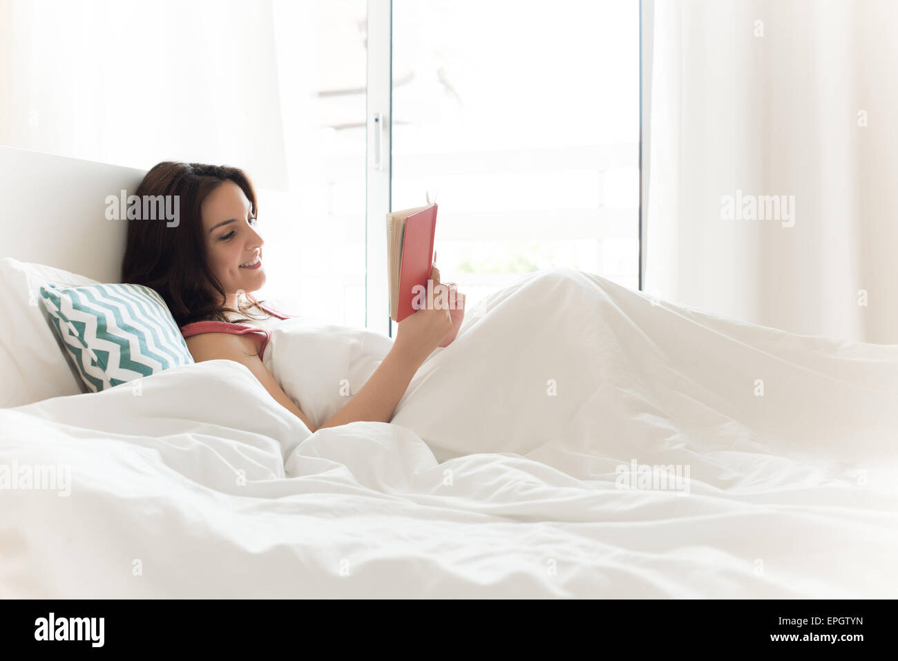 Woman reading book in bed during the morning Stock Photo