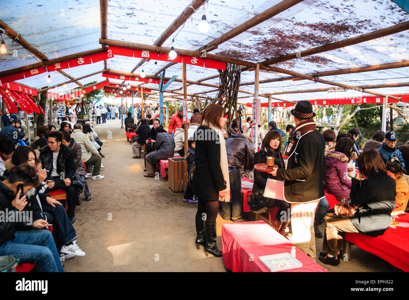 People sitting in coats at tables during the new year festival in covered outdoor eating area at the Nishinomiya Shinto shrine in japan. Stock Photo