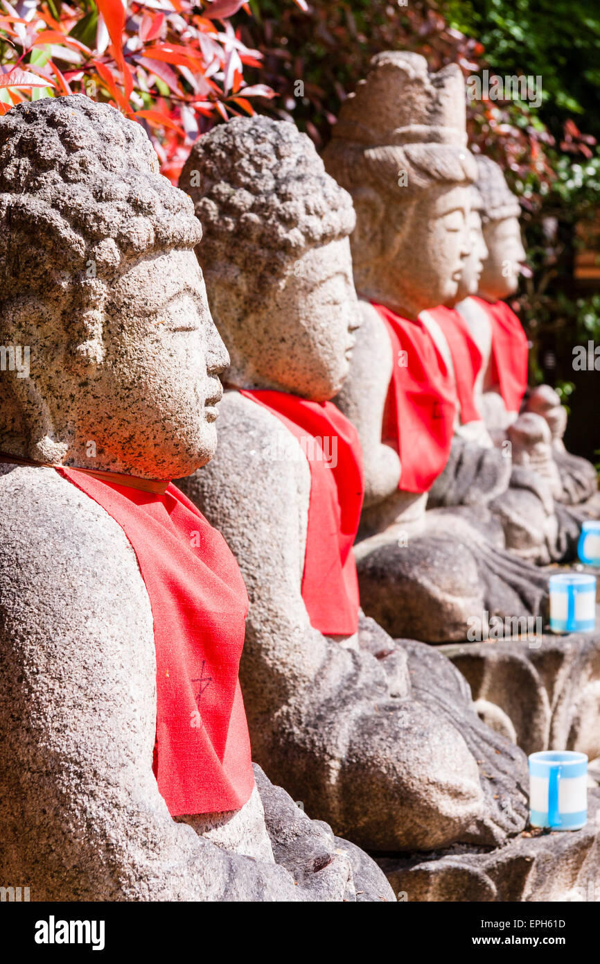 Close up view along four sitting Jizo bosatsu statues with red bibs in asunlight, outdoors at