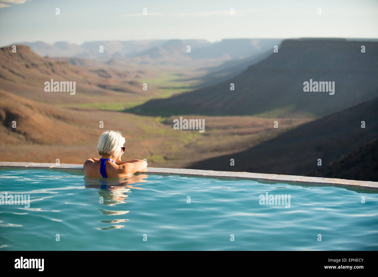 Africa, Namibia. Grootberg Lodge. Woman looking off into distance, relaxing in swimming pool. Stock Photo