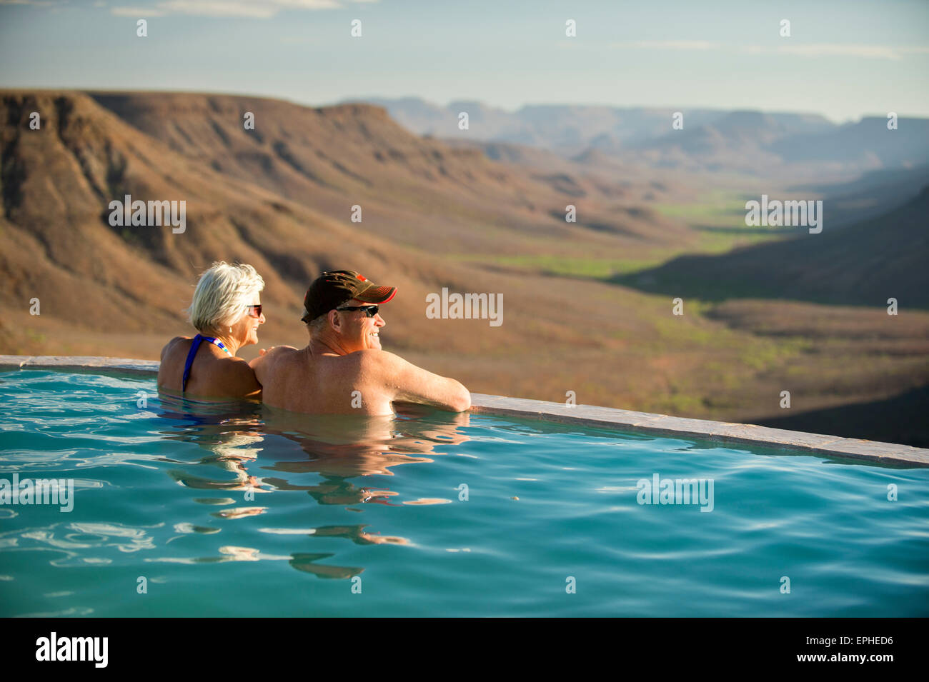 Africa, Namibia. Grootberg Lodge. Man and woman looking off into distance, relaxing in swimming pool. Stock Photo