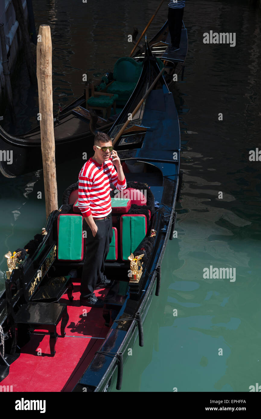 VENICE, ITALY - APRIL 24, 2013: Venetian gondolier in traditional red and white striped shirt talks on his mobile phone. Stock Photo