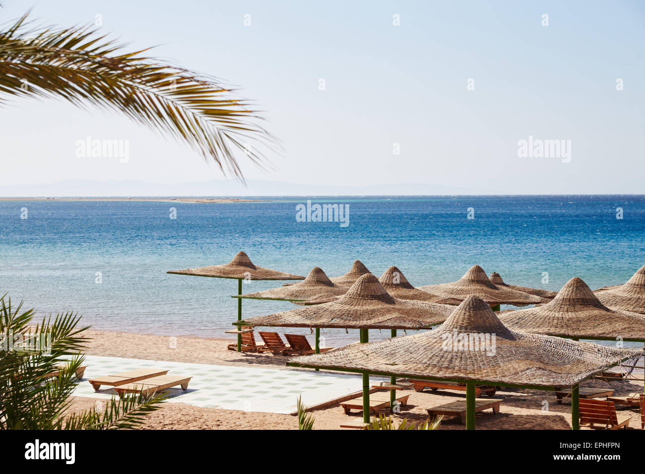 Beach, Red Sea, umbrellas, chaise lounges, branches of date palms against the blue sky, lots of sun Stock Photo