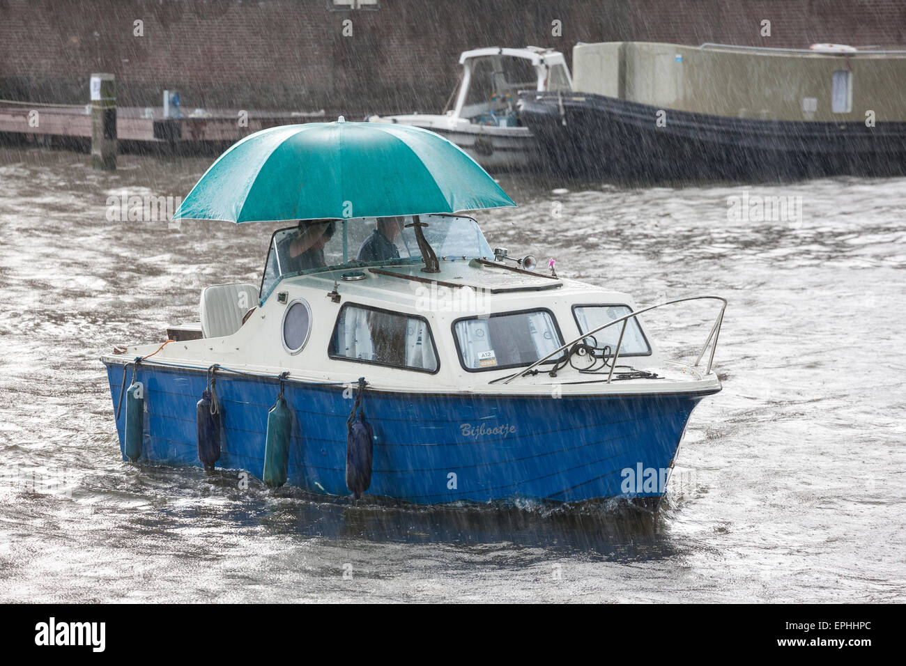 Amsterdam raining. Small boat, small cabin cruiser in sudden summer rain with large umbrella in Amsterdam canal Stock Photo