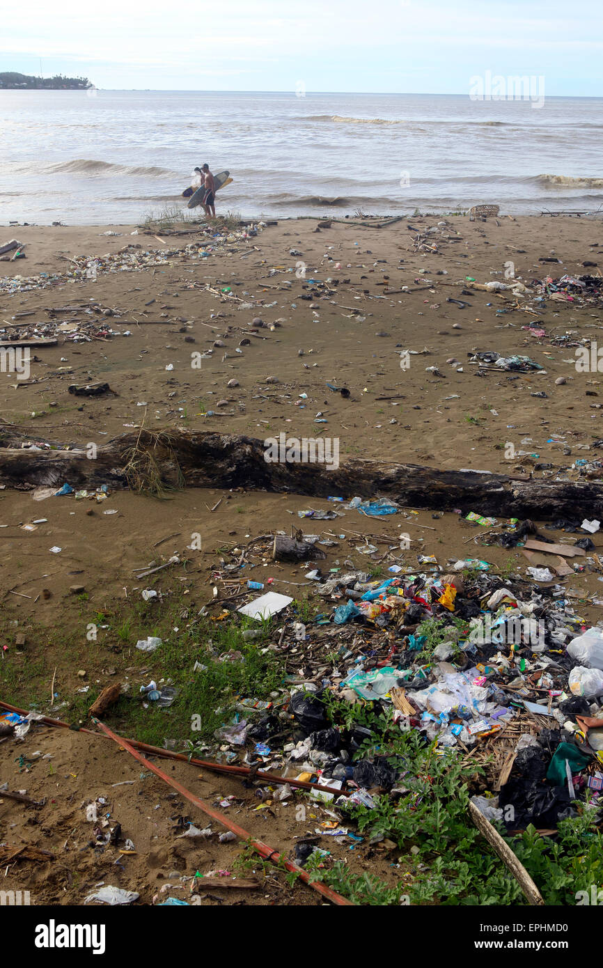 Surfers walk along beach covered in plastic trash and other garbage in