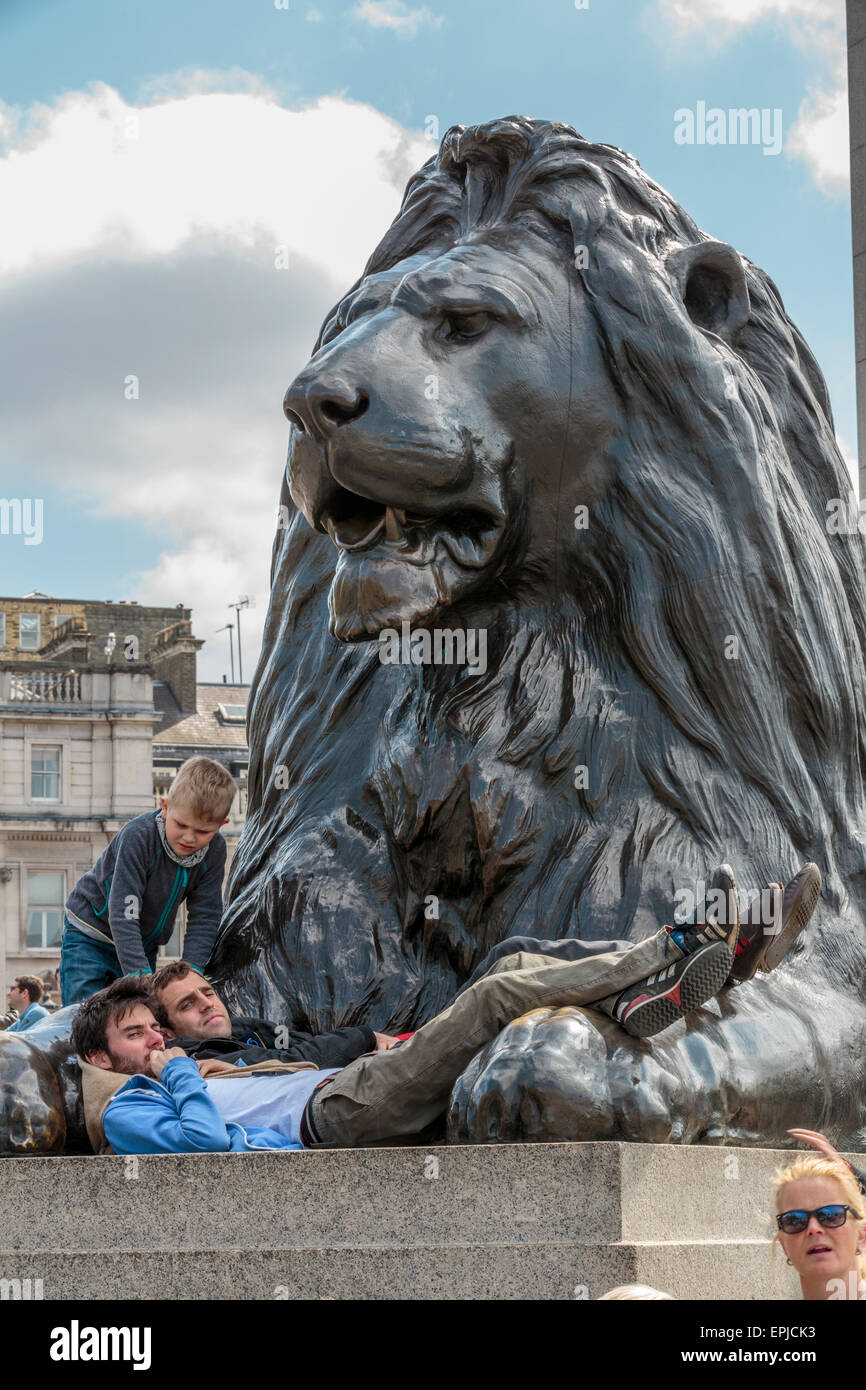 Portrait image of a young boy looking at 2 tourists laying on a lion at Trafalgar Square, London, UK Stock Photo