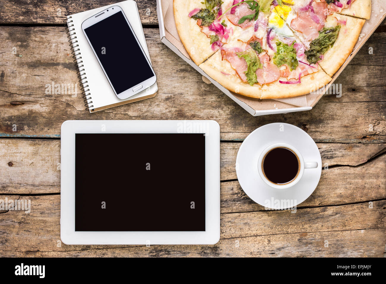 Remote freelance workplace coffee break. Outsource workspace with tablet PC, smartphone and pizza with coffee. Top view image Stock Photo