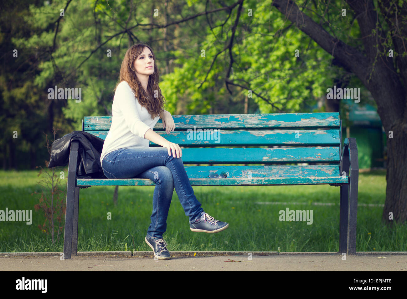 Young beautiful woman sitting on bench in park. Pretty girl at outdoors on summer day. Nature environment background. Stock Photo