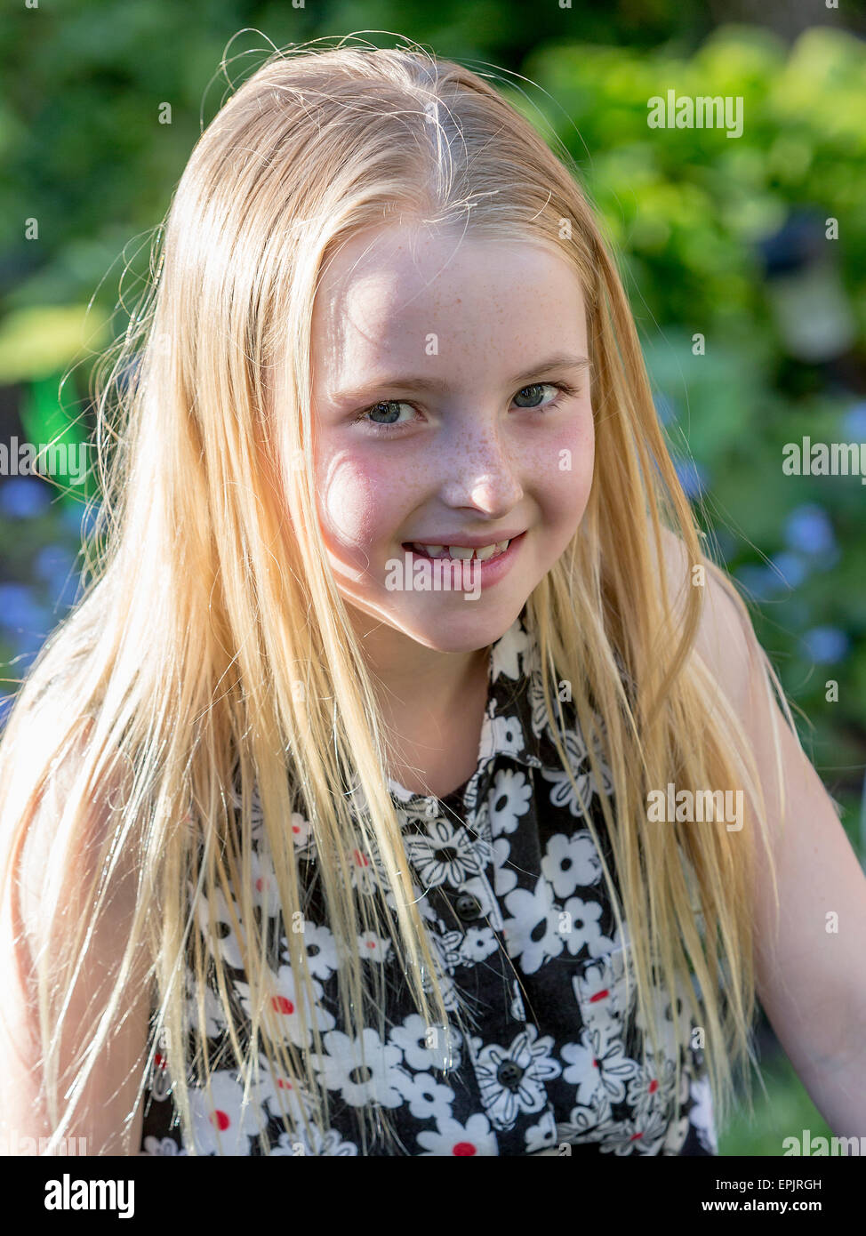 Blonde 8 year old girl sitting in a garden posing for the camera Stock Photo