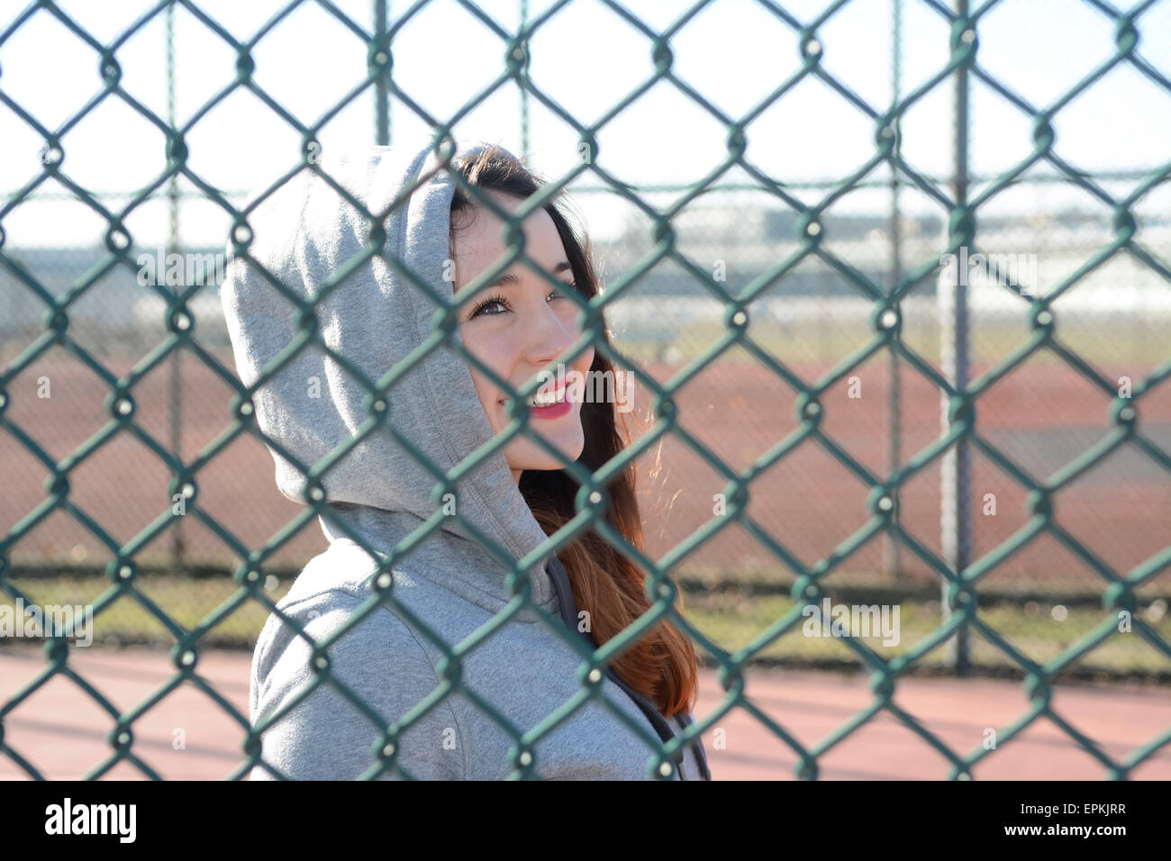 Portrait of woman wearing hooded jacket behind mesh wire fence Stock Photo Alamy