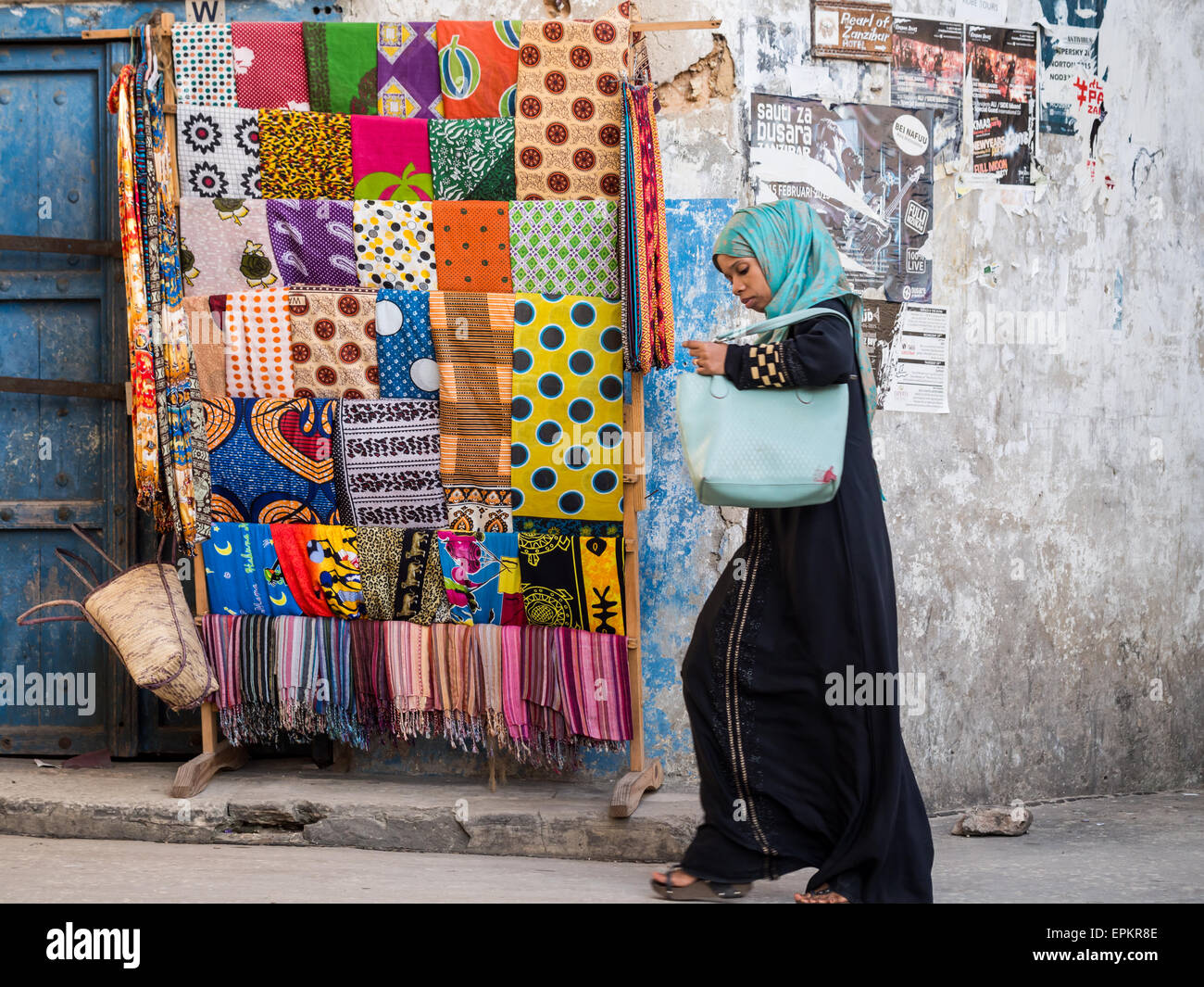 Woman walks next to a rack with colorful garments called kanga and kitenge in Stone Town, Zanzibar. Stock Photo