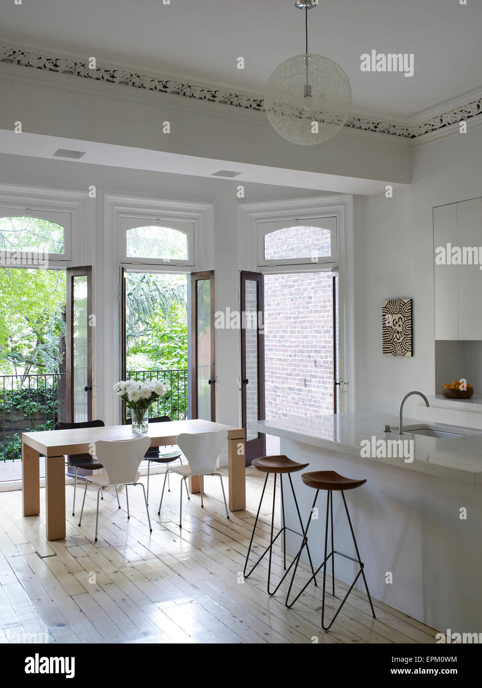 Breakfast bar, stools and small dining table in white kitchen with open glass doors leading to garden, Chelsea Townhouse, New York, USA Stock Photo