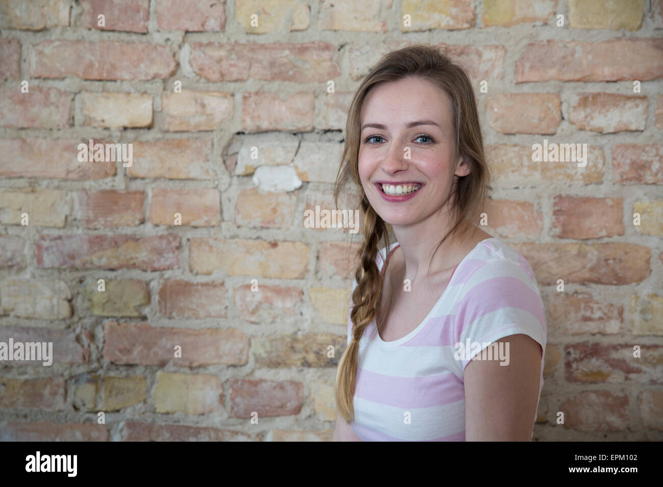 Portrait of smiling young woman in front of brick wall Stock Photo - Alamy